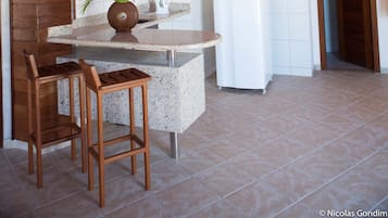 Una cocina con vigas de madera en el techo, un refrigerador blanco, un microondas, una pequeña mesa con dos sillas de madera y una planta en maceta.