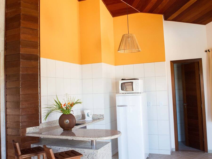 Una cocina con vigas de madera en el techo, un refrigerador blanco, un microondas, una pequeña mesa con dos sillas de madera y una planta en maceta.