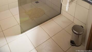 A bathroom with a glass-enclosed shower, a sink with a granite countertop, and a trash can.