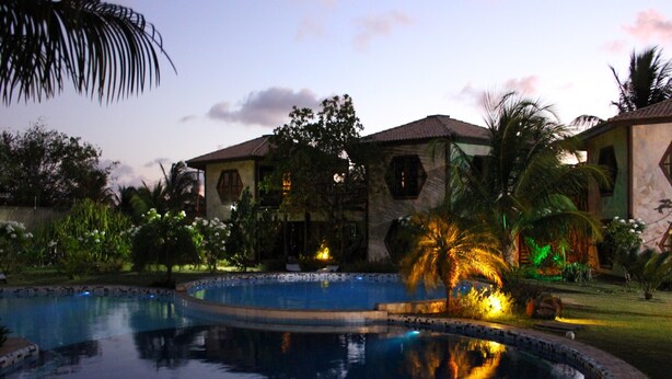 A pool surrounded by a landscaped garden with palm trees and a building with a tiled roof.