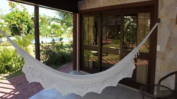 A hammock hanging over a tiled patio with a glass door leading to a garden.