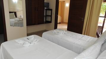 Quarto de hotel com duas camas, televisão sobre um suporte, espelho e porta que dá para outro cômodo.