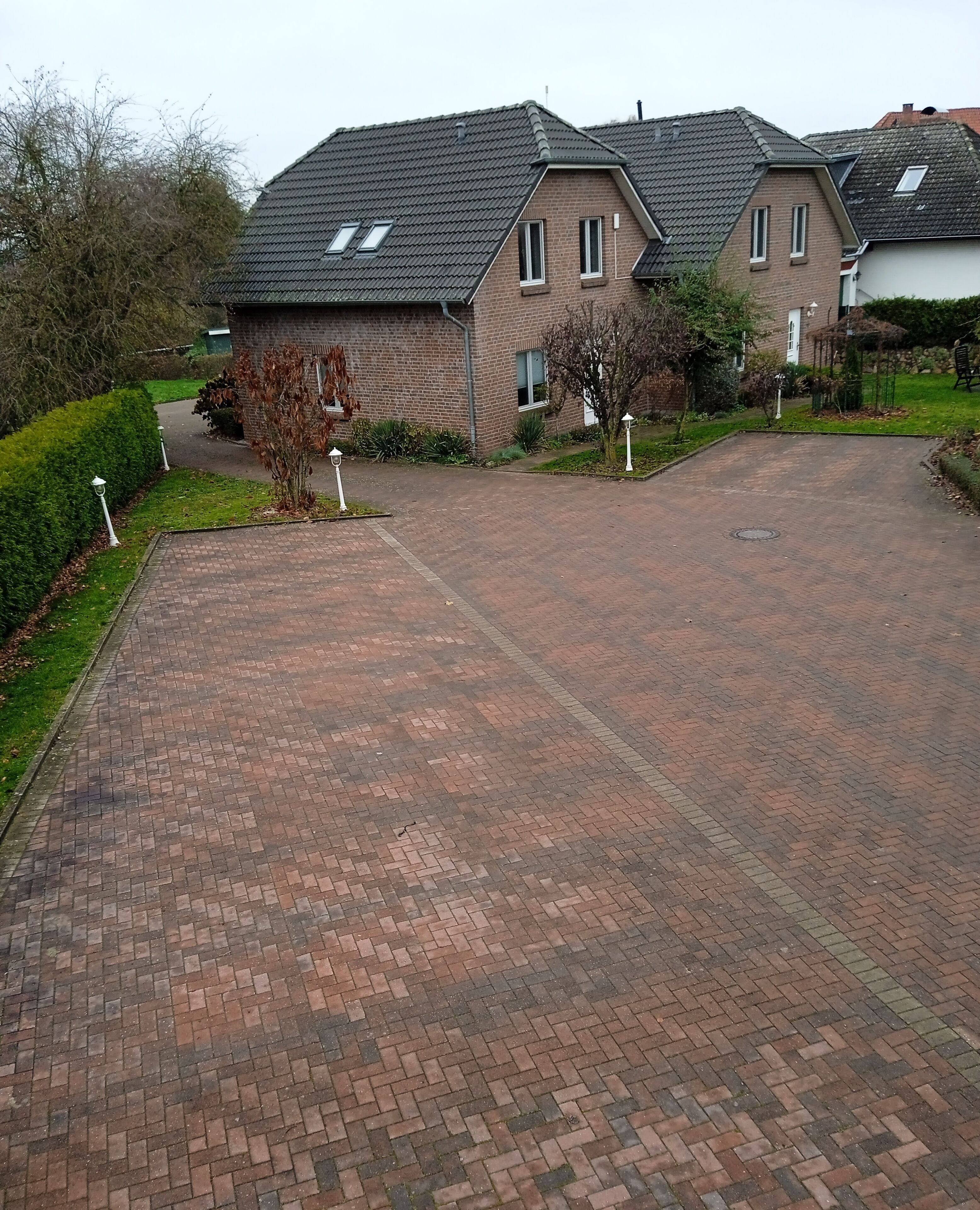 A residential driveway leading to a brick house with a sloped roof and a small garden area.