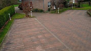 A residential driveway leading to a brick house with a sloped roof and a small garden area.