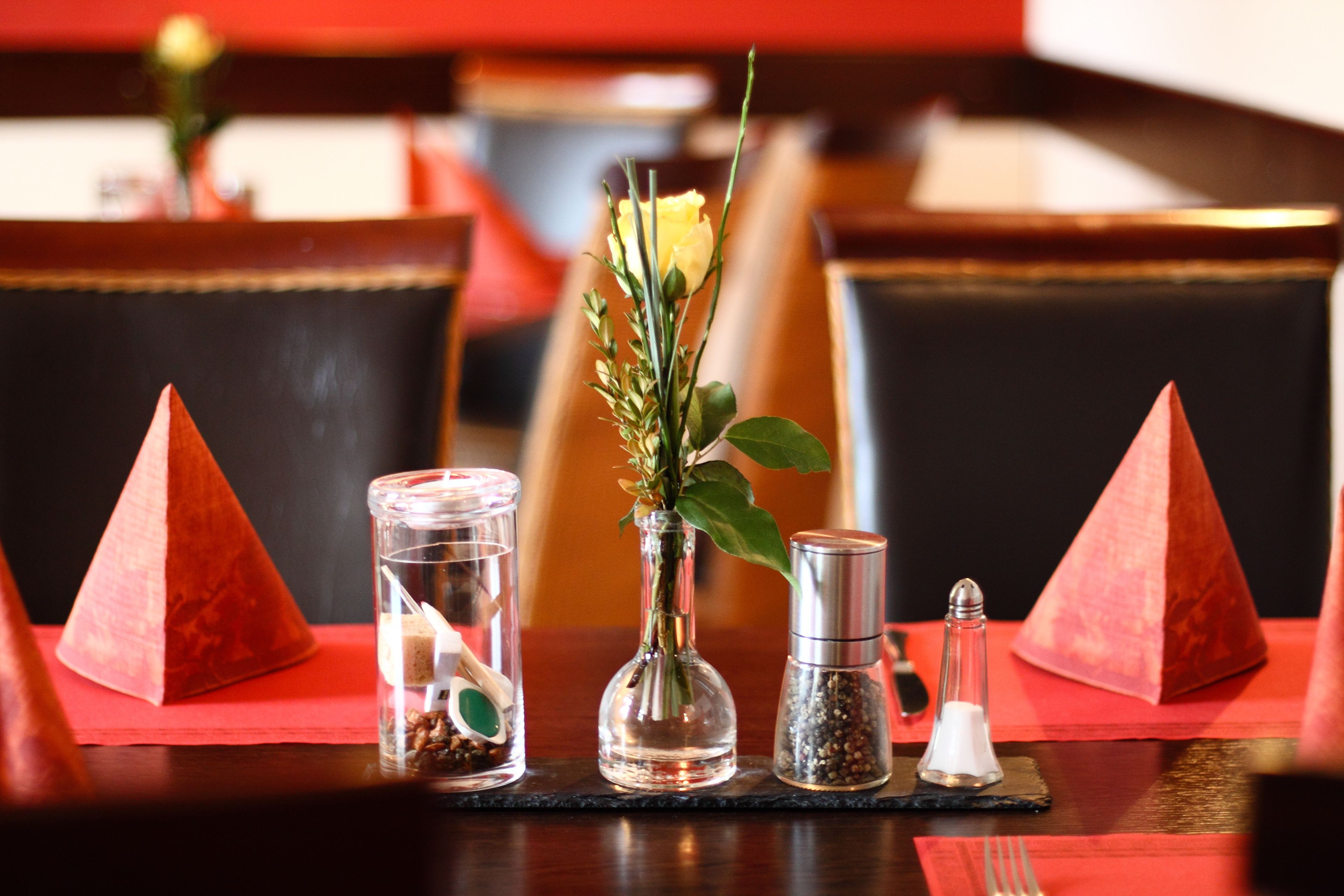 Una mesa de comedor con un jarrón de rosas amarillas, saleros y pimenteros, y un recipiente de vidrio con una cuchara.