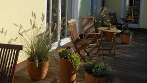 Un patio con mobiliario exterior, plantas en macetas y un edificio con ventanas amplias y un balcón.