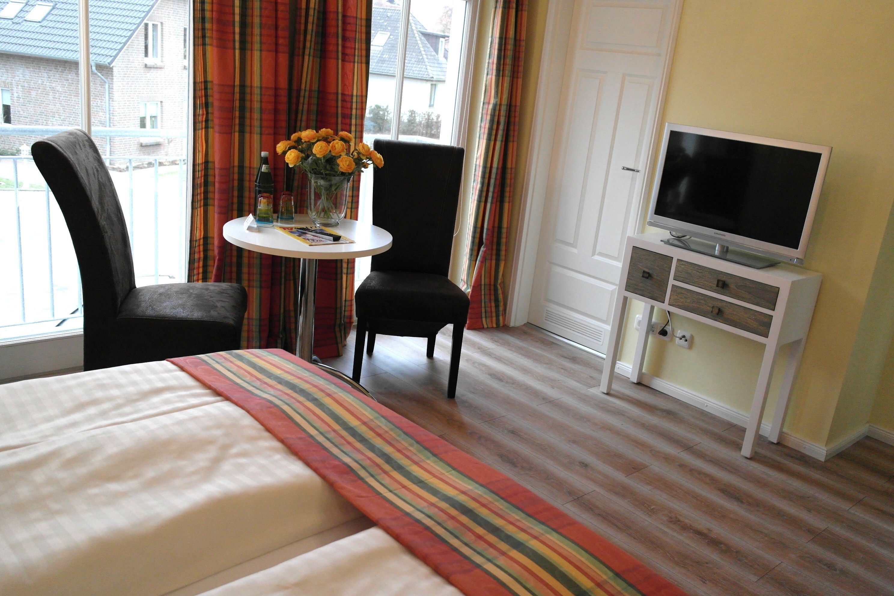 Ein Hotelzimmer mit einem Bett, einem Fernseher auf einem Schrank, einem kleinen Tisch mit Blumenvase und zwei Stühlen.