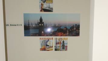 A room with a wooden floor, a white console table with drawers, and wall-mounted pictures of Hamburg and other locations.