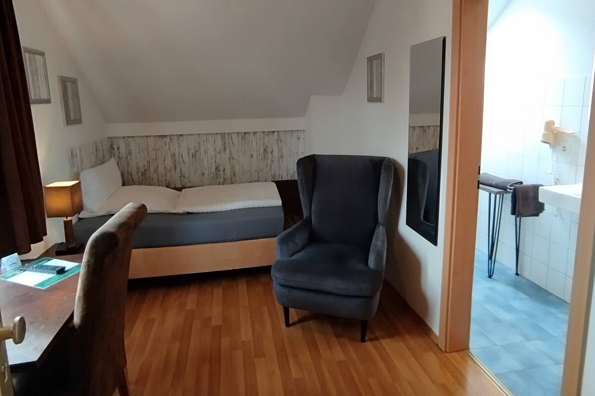 Habitación compacta con cama, escritorio, silla y televisor montado en la pared.