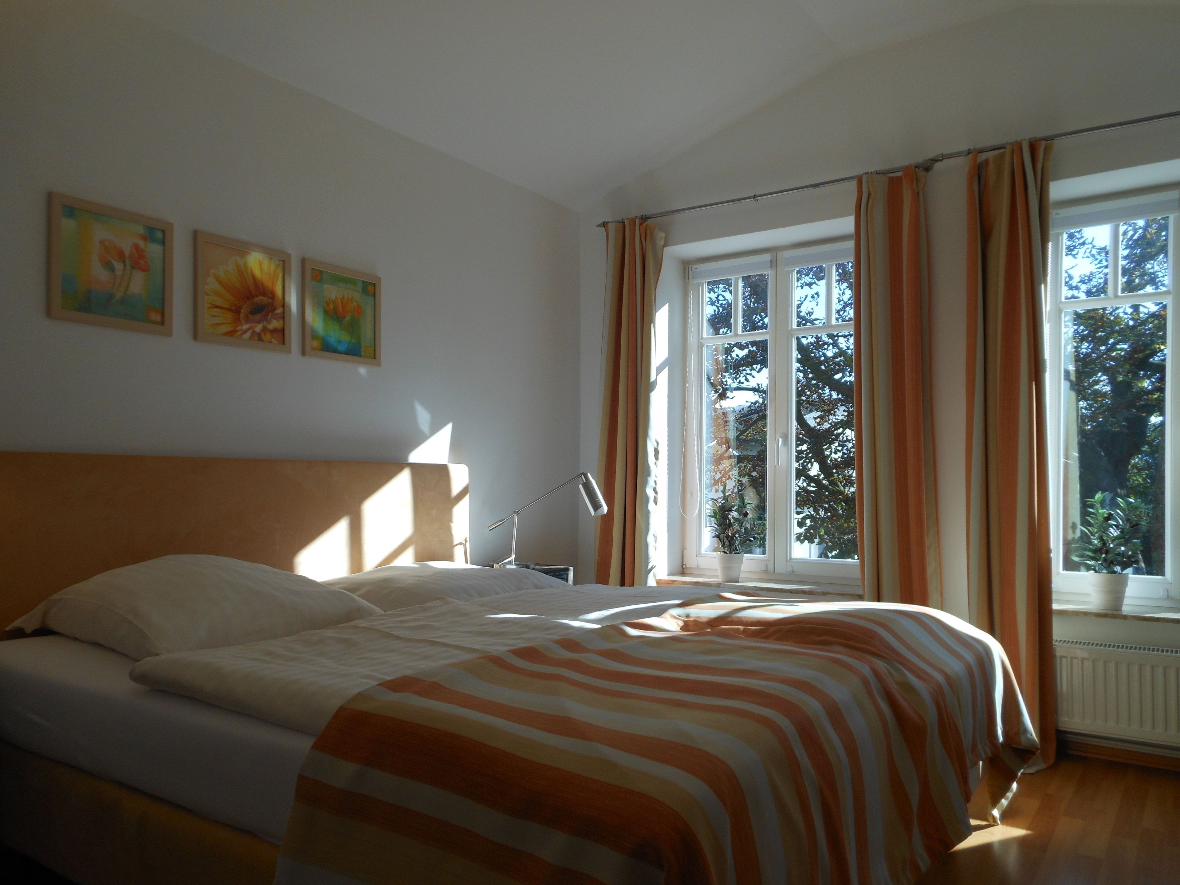 Een slaapkamer met een bed, nachtkastje, lamp en een raam met gordijnen.