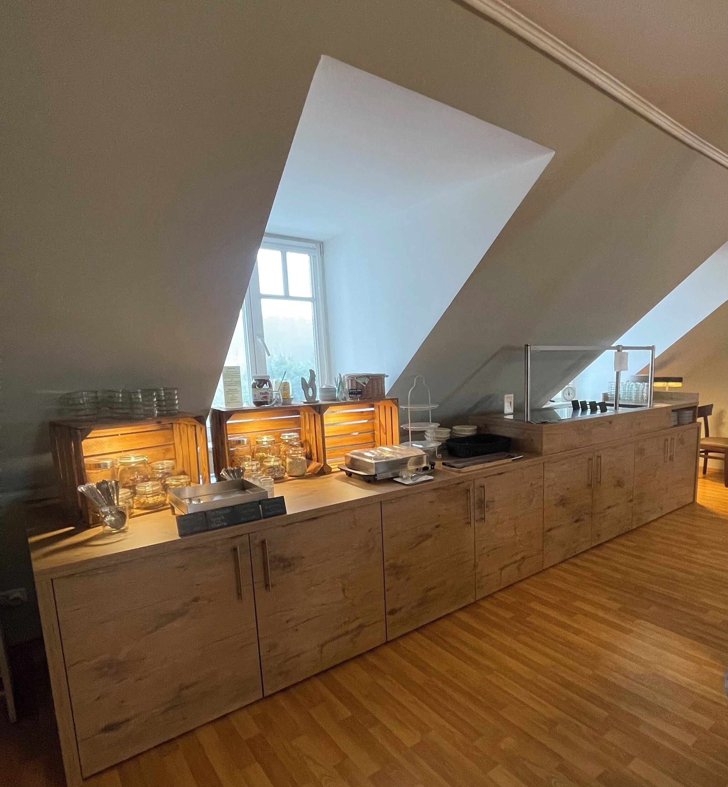 A long, wooden counter with glass jars and utensils, a window, and a high ceiling with skylights.