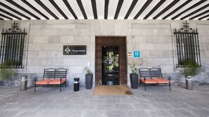 A hotel entrance with a stone facade, a wooden door, and two benches with orange cushions. - Arrupe (Azpeitia)