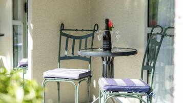 Un balcón en esquina con una mesa y dos sillas, una botella de vino y una copa.
