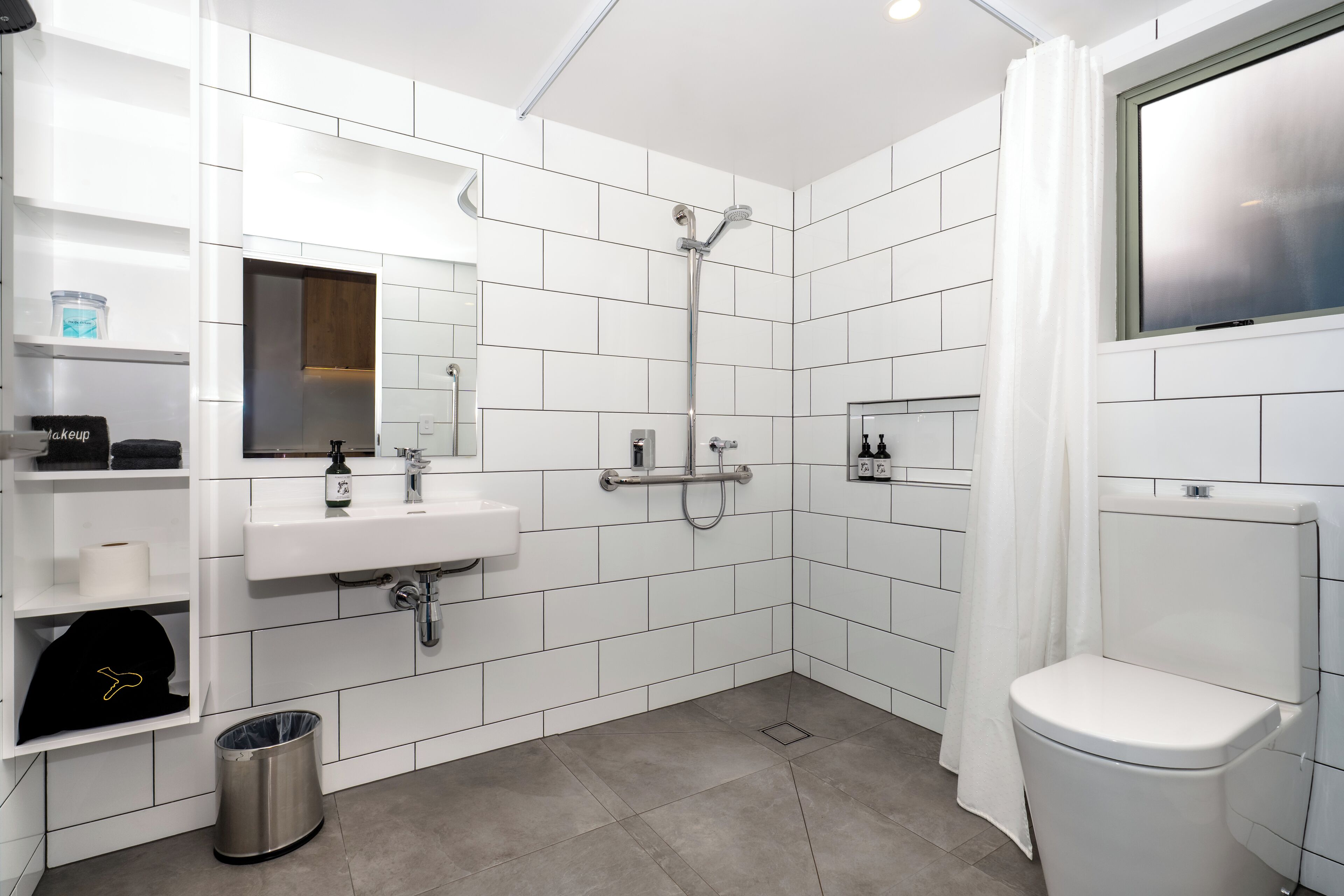 Un baño moderno con azulejos blancos, un lavabo, un inodoro y una ducha.