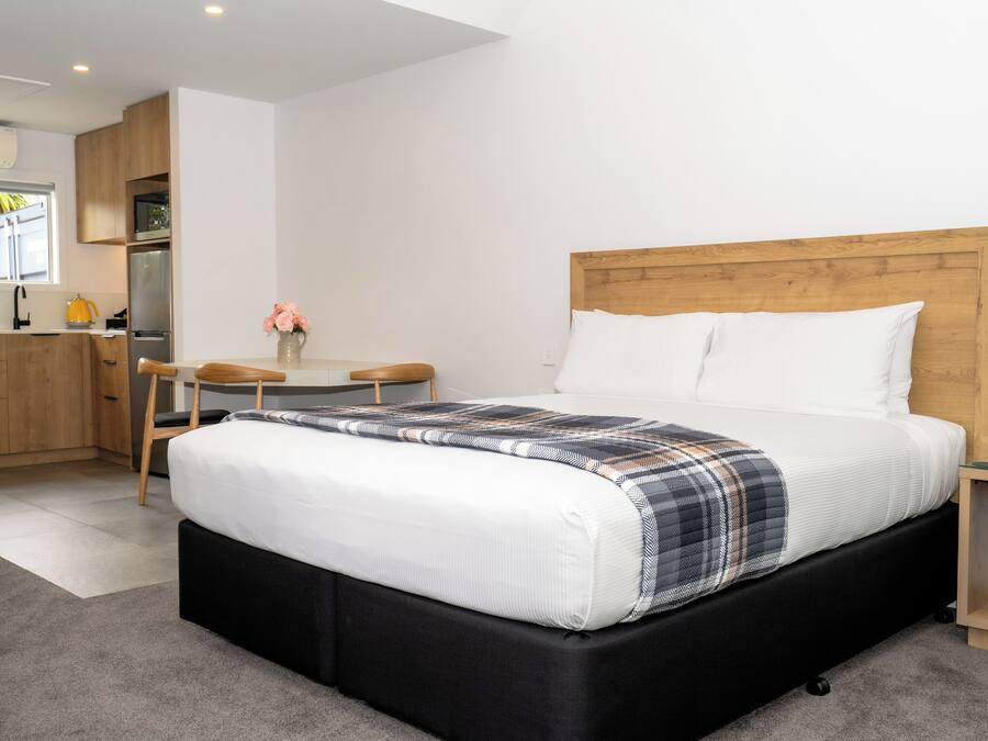 A modern bedroom with a large bed, a wooden headboard, and a small bedside table.
