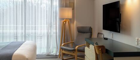 Habitación de hotel con cama, escritorio y silla, televisión montada en la pared y lámpara.