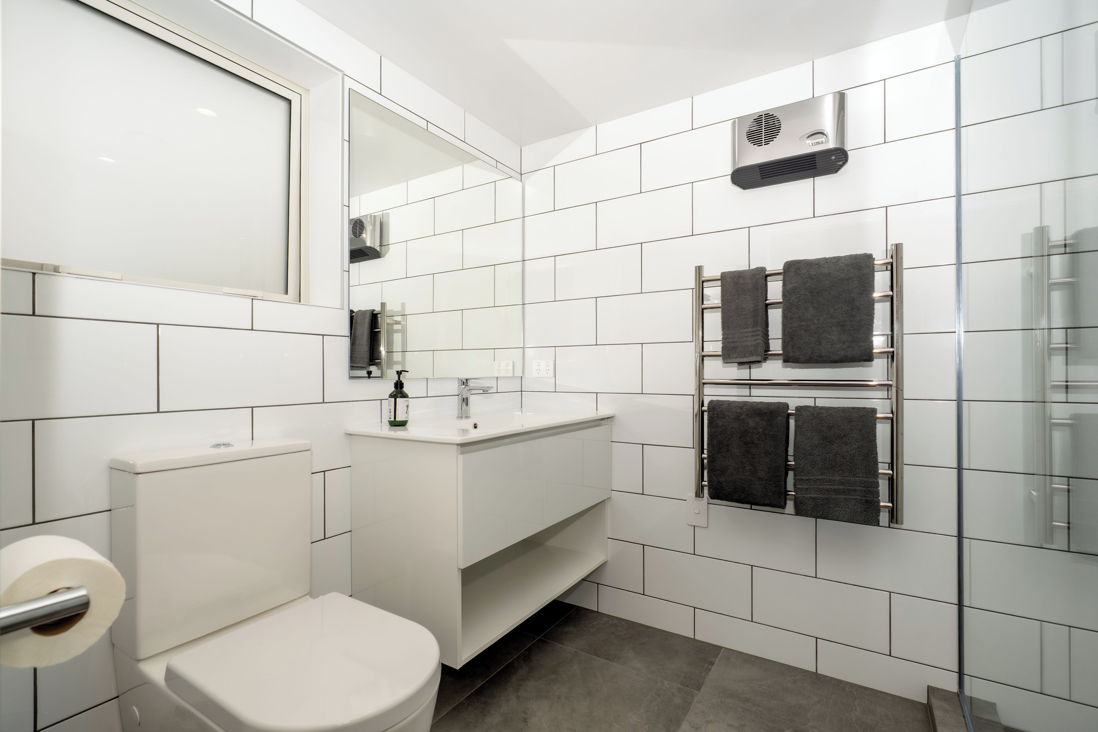 A modern bathroom with white tiles, a toilet, a sink, and a towel rack.