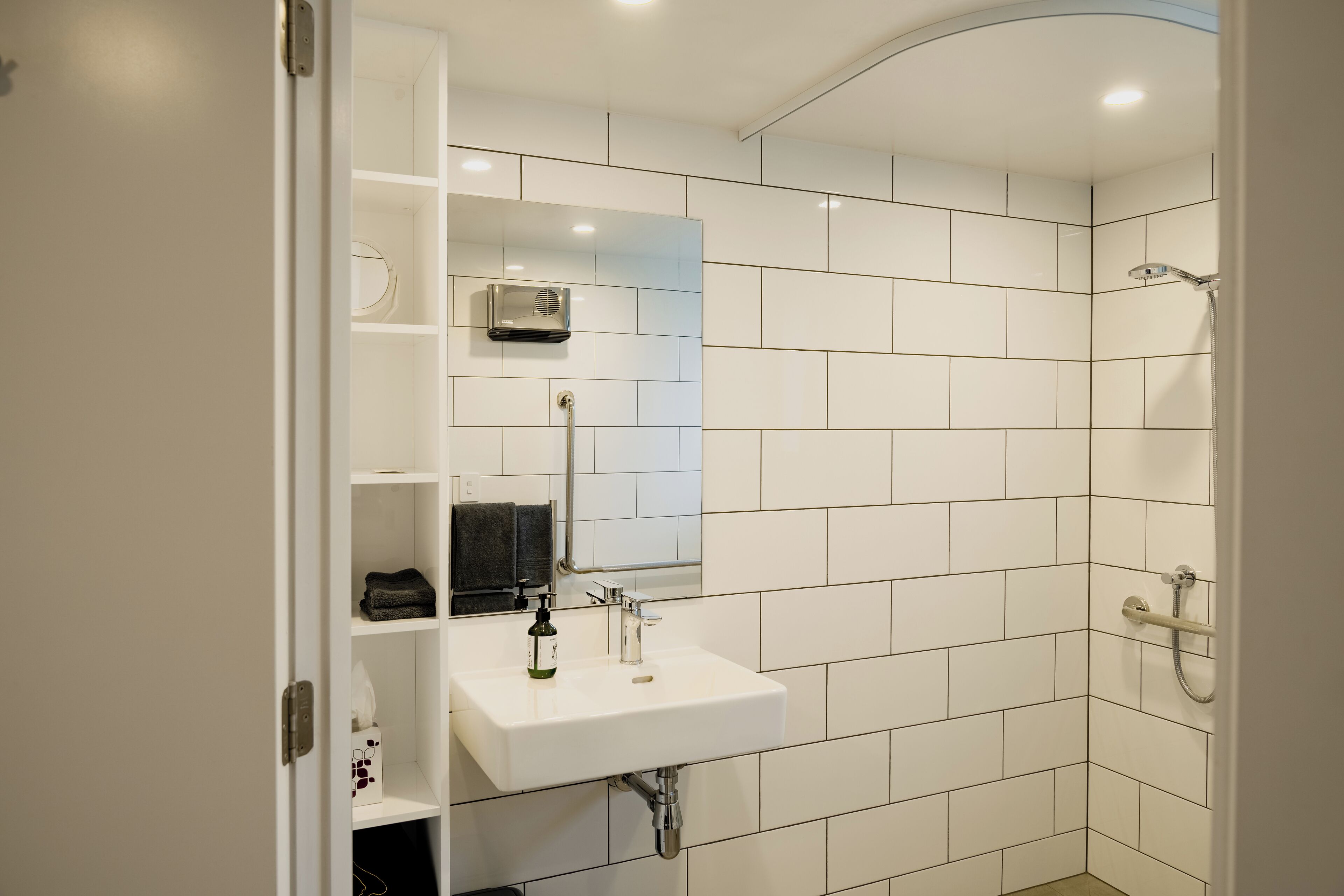 A modern bathroom with white tiles, a sink, a mirror, and a shower.