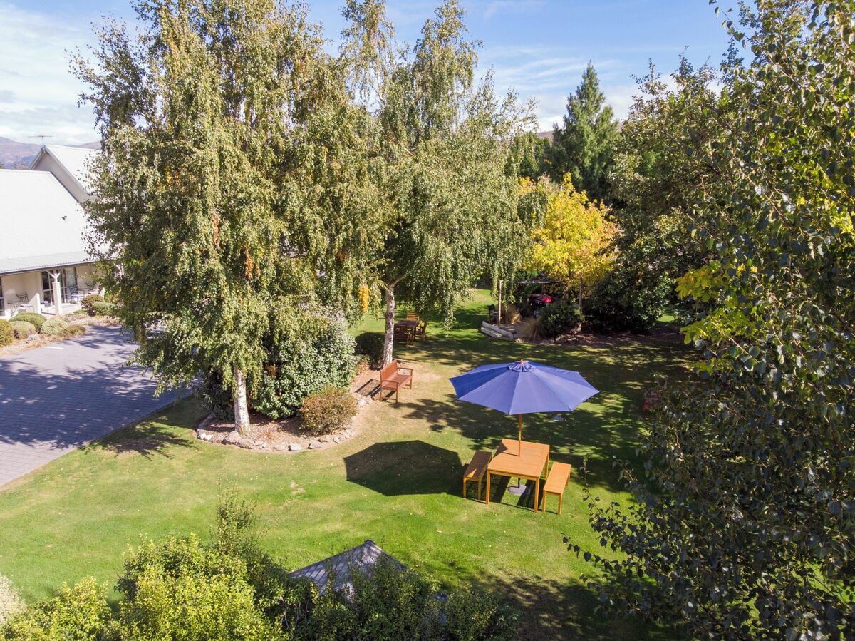 Un jardín bien cuidado con césped, una mesa y sillas de madera, y una sombrilla azul.