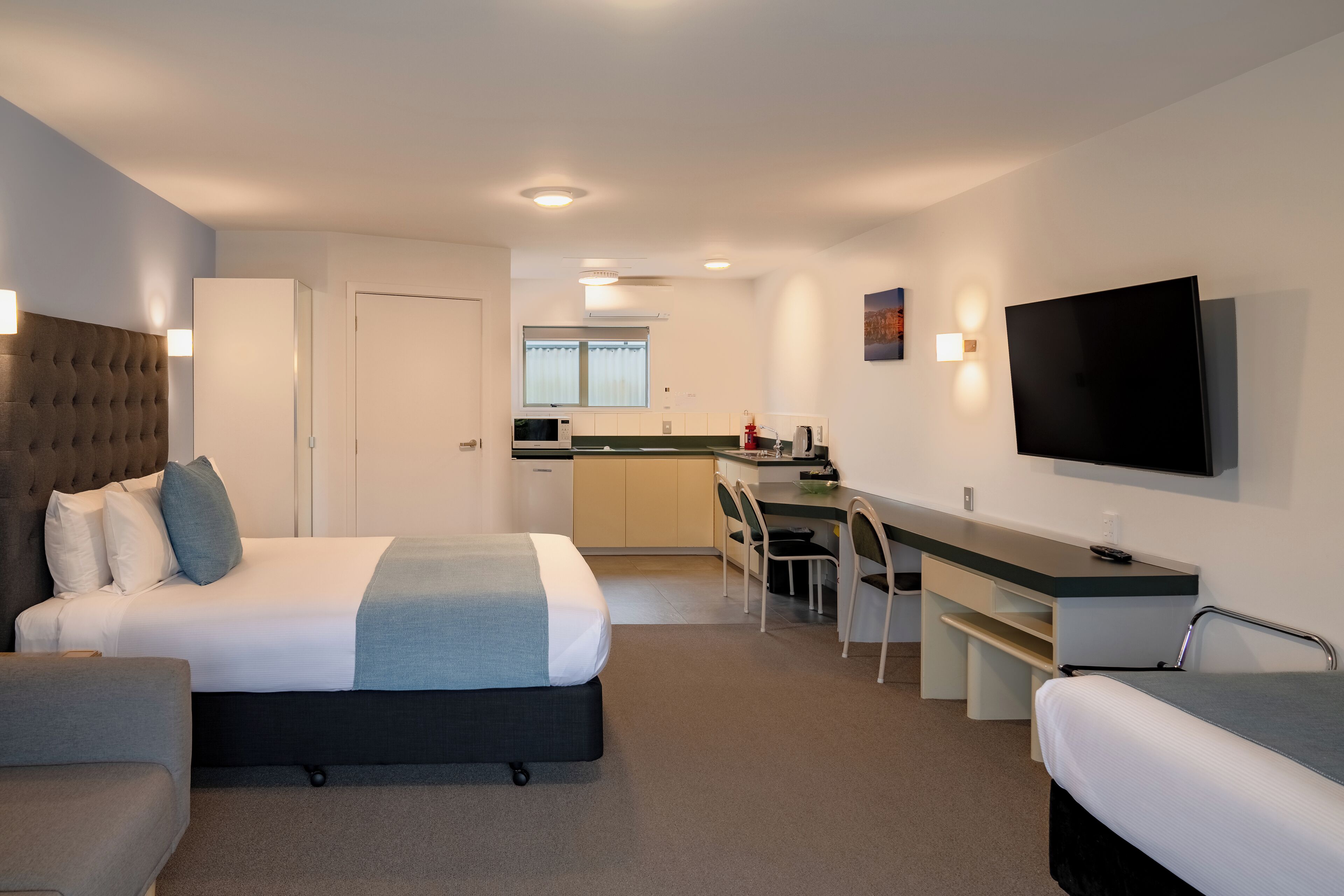 Une chambre d’hôtel moderne équipée d’un lit, d’un bureau, d’une chaise, d’une télévision et d’une kitchenette.