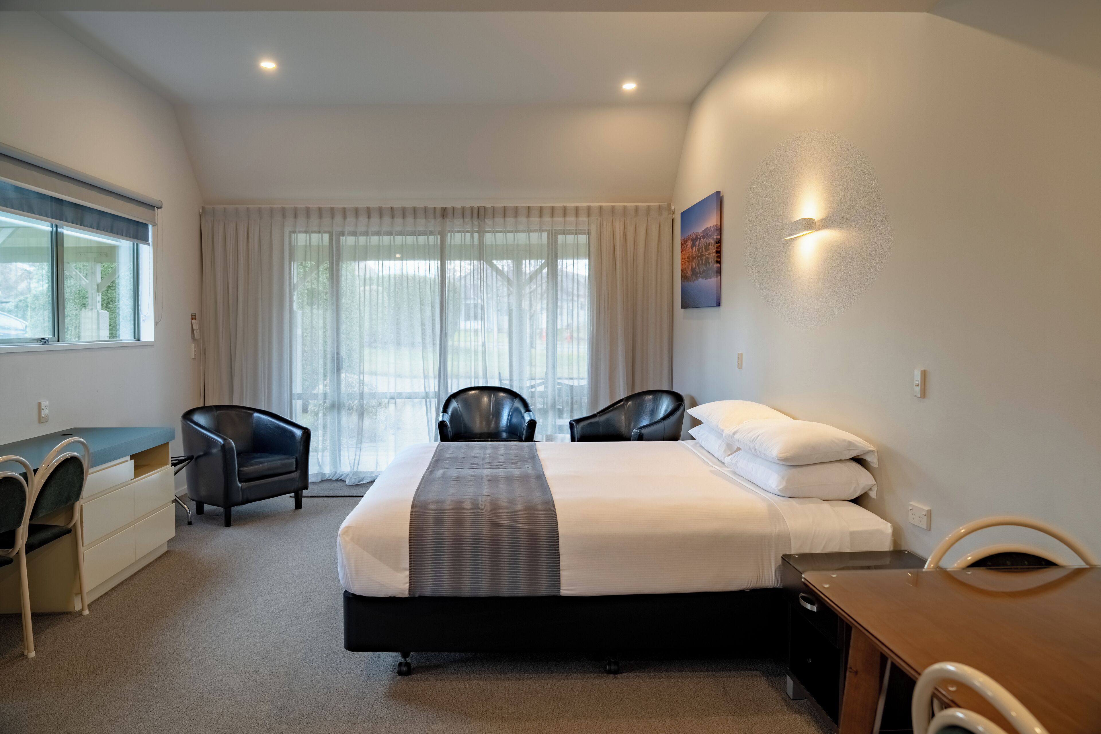 Ein Hotelzimmer mit einem Bett, zwei Stühlen, einem Schreibtisch und einem Fenster mit Vorhängen.