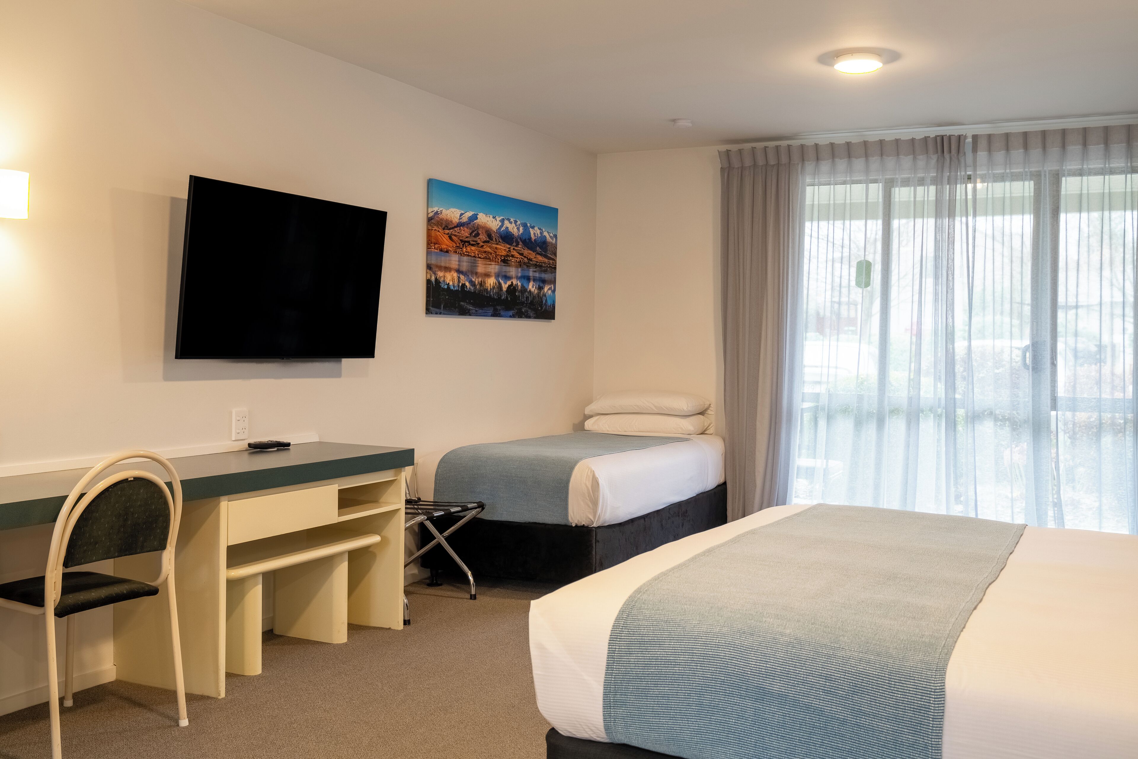 A hotel room with a bed, a desk, a chair, a television, and a window with curtains.