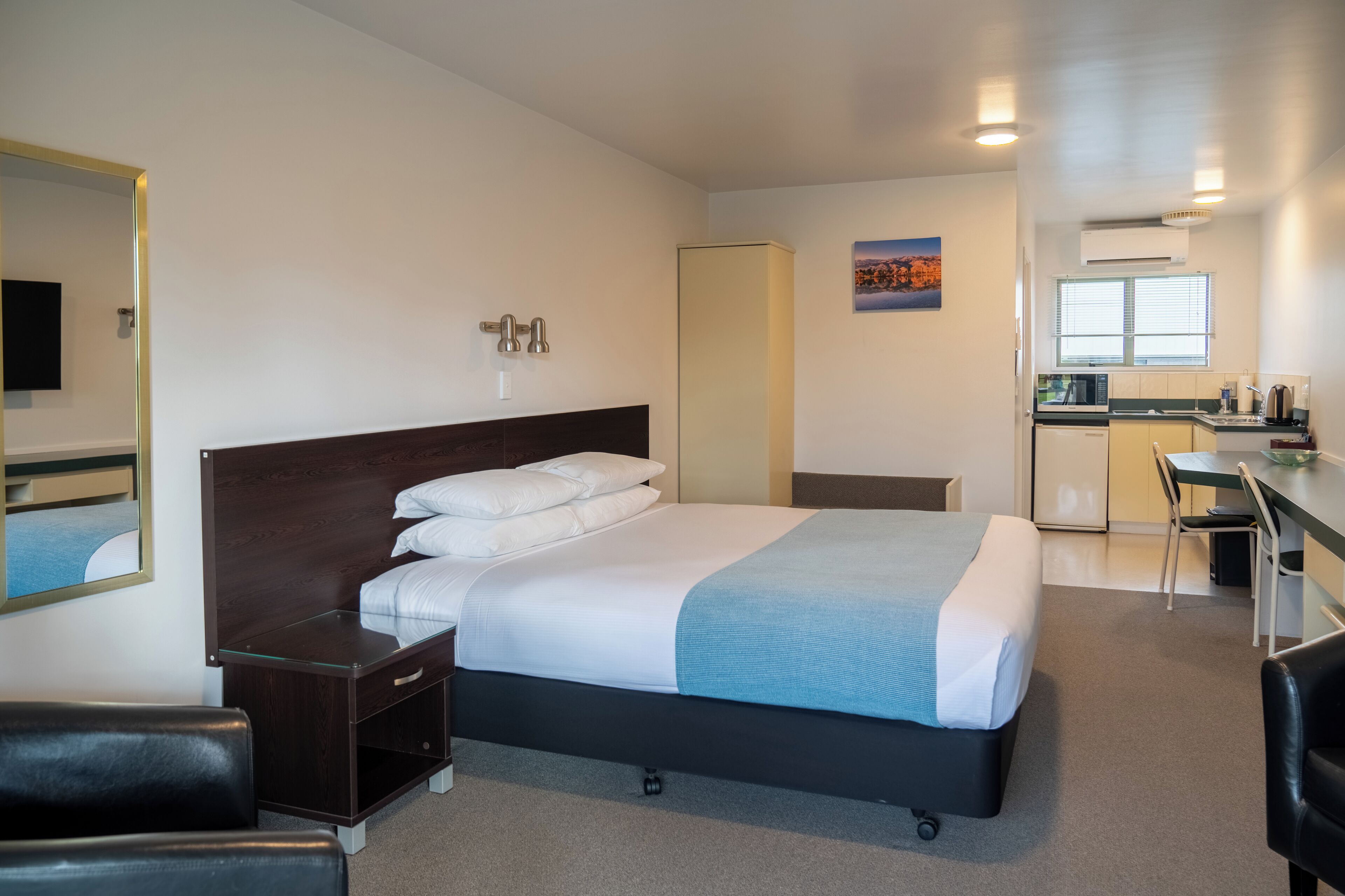 Une chambre d’hôtel comprenant un lit, un bureau, une chaise, une armoire et une kitchenette.