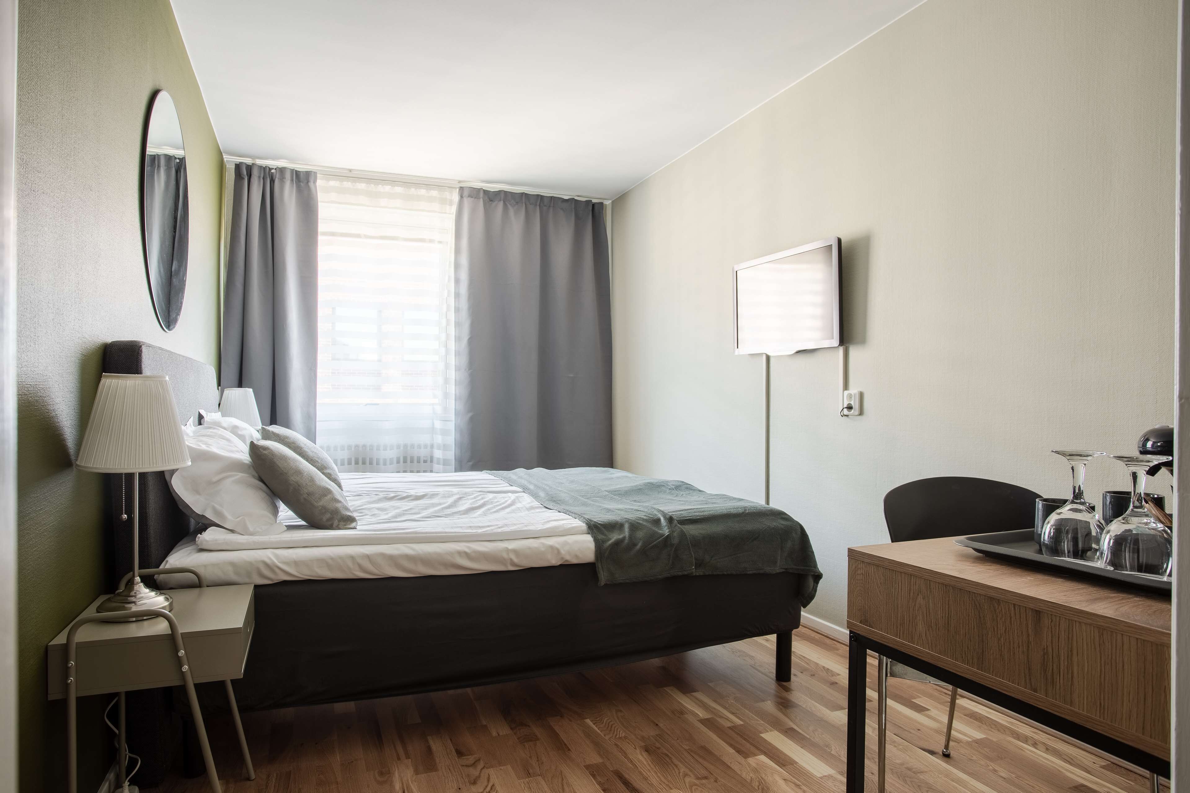 Een moderne hotelkamer met een bed, nachtkastje, lamp en een bureau met een dienblad glazen.