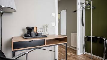 Una habitación con escritorio de madera, una silla, una lámpara, un radiador y un perchero.