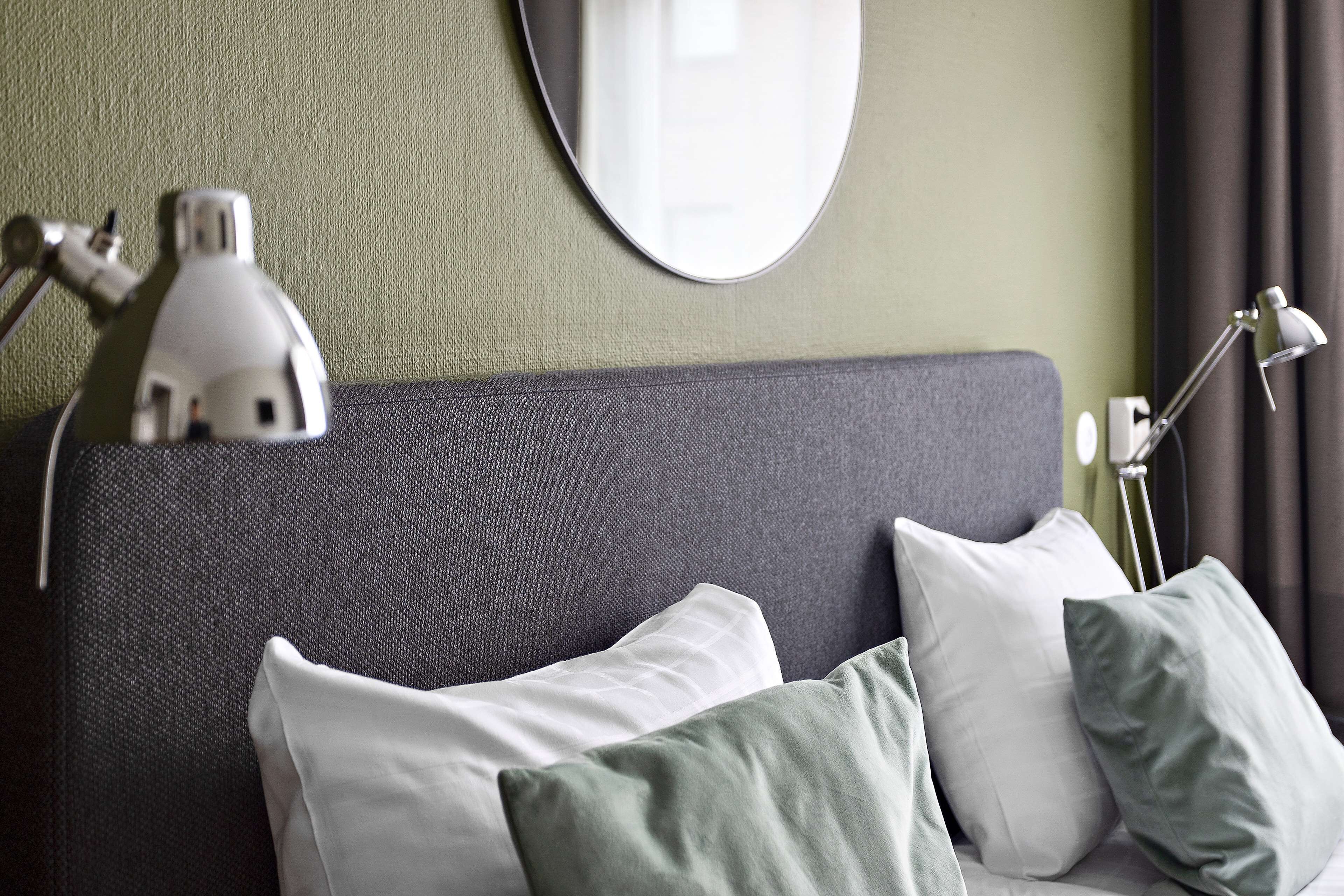 Un lit bien fait, avec des oreillers, une lampe de chevet et un miroir fixé au mur.