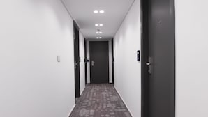 Un couloir avec un tapis à motifs, des murs blancs et des portes sombres.