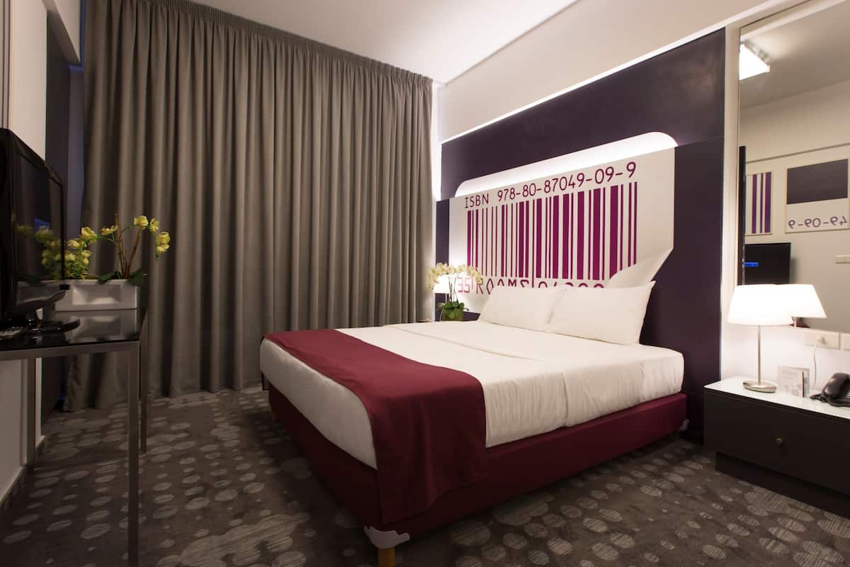 Ein Hotelzimmer mit einem großen Bett, einem Schreibtisch, einem Stuhl, einer Lampe und einem Spiegel.