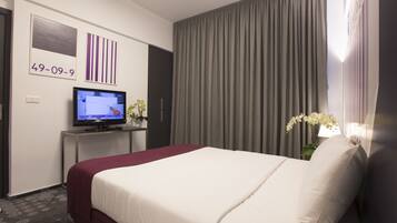 A hotel room with a large bed, a television on a desk, and a window with curtains.