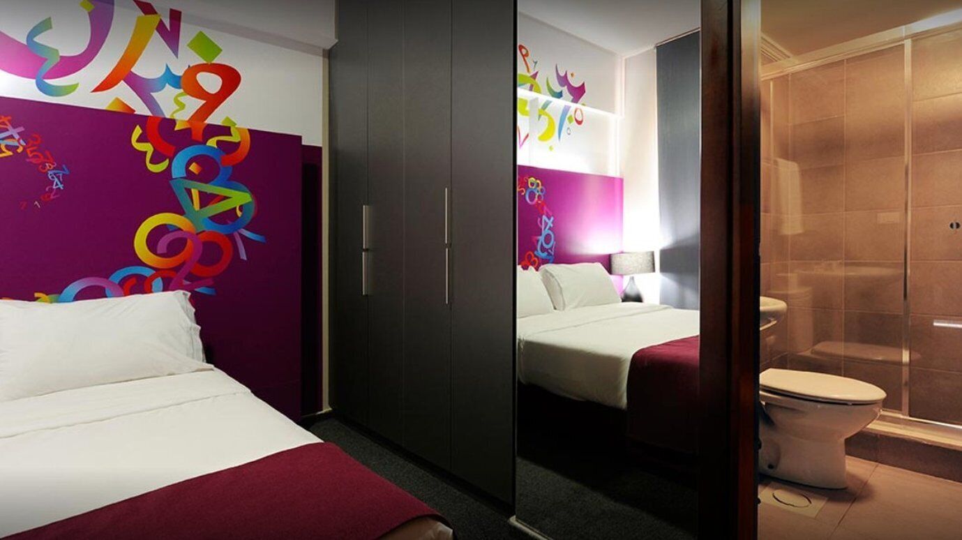 A hotel room with a bed, a wardrobe, a bathroom with a shower, and colorful wall art.