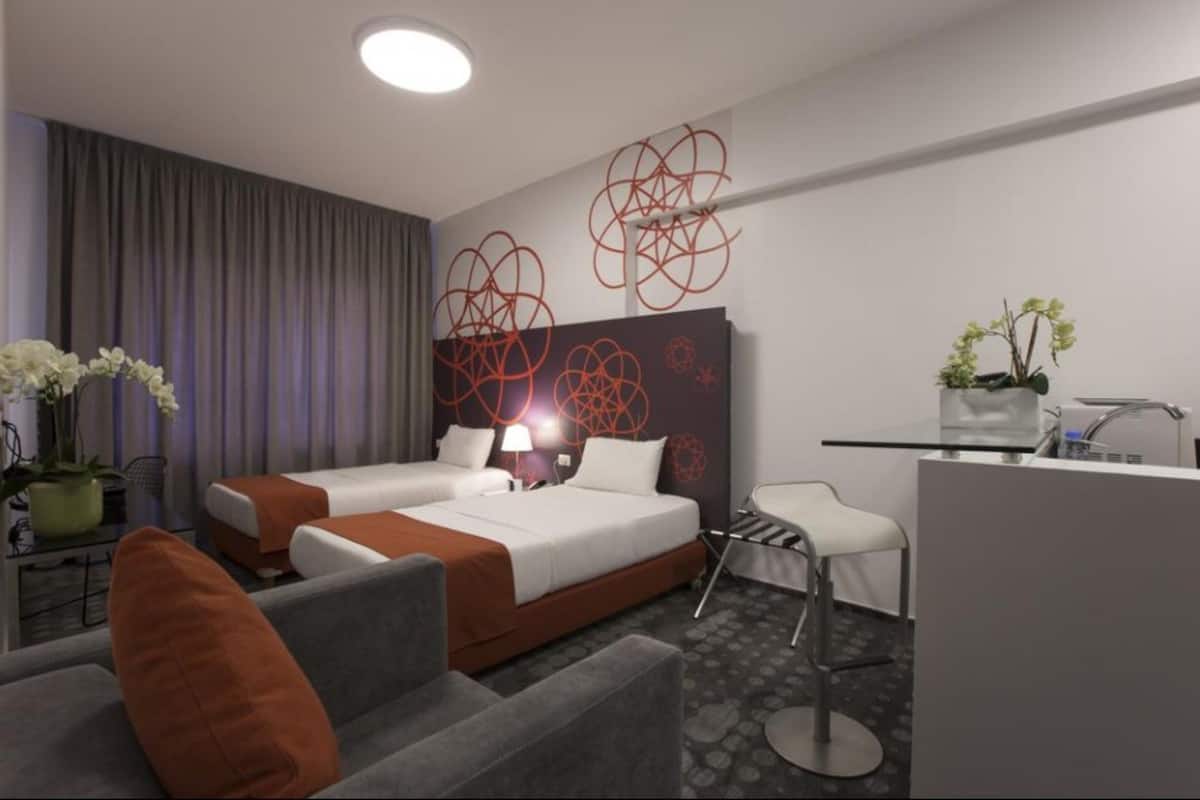 Ein modernes Hotelzimmer mit zwei Betten, einem Schreibtisch, einem Stuhl und einer Zimmerpflanze.