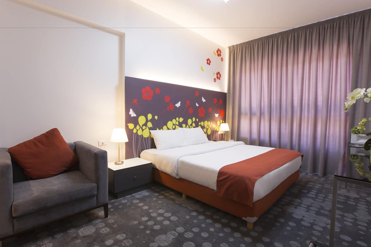 Ein Hotelzimmer mit Bett, Sofa, Nachttisch, Lampe und einem fenster mit Vorhängen.