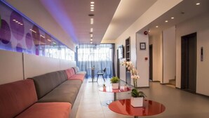 Un hall d’entrée moderne avec un long canapé rouge, une table basse en verre et une plante en pot.