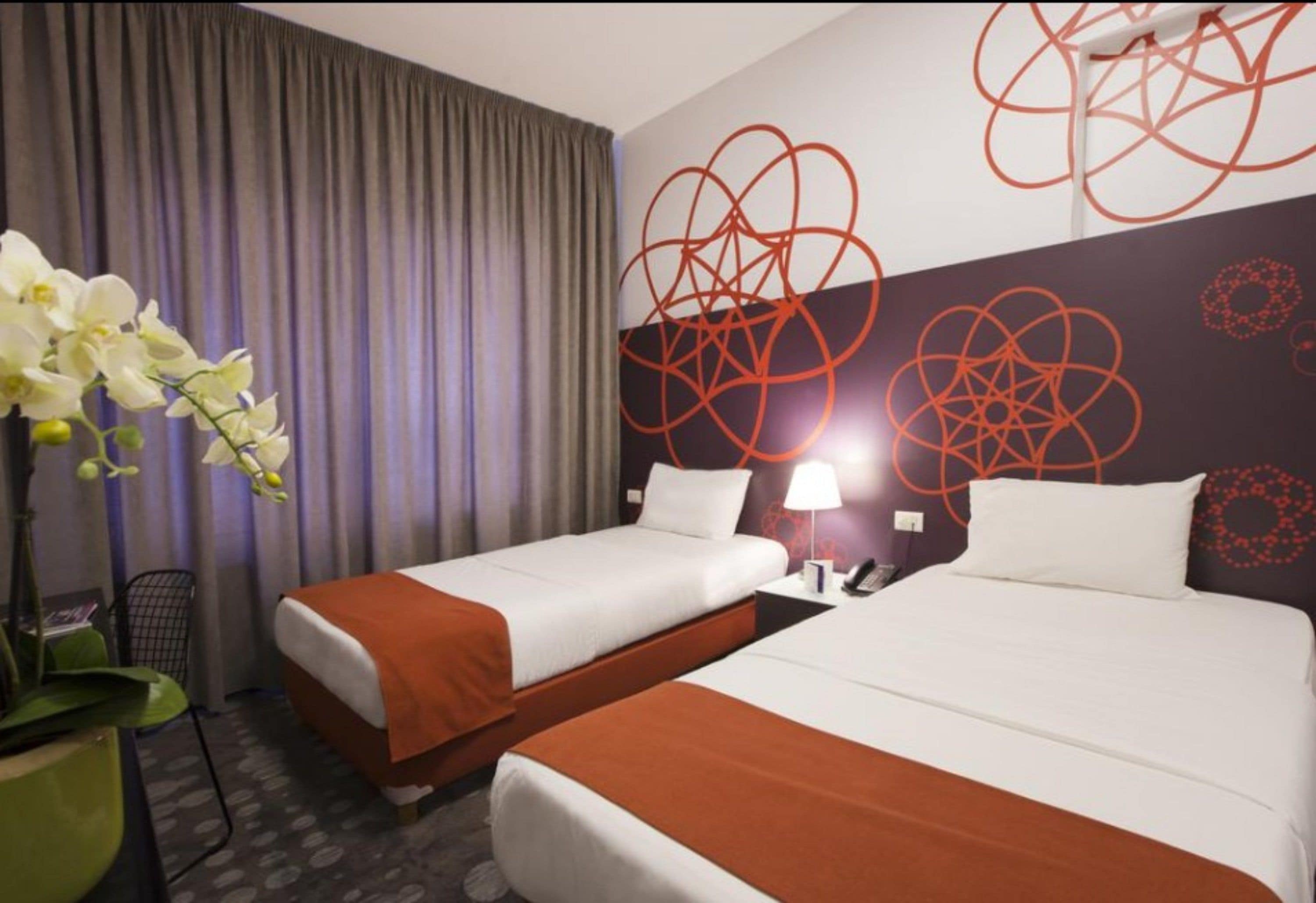 Une chambre d’hôtel avec deux lits, un bureau, une chaise et une grande fenêtre avec des rideaux.