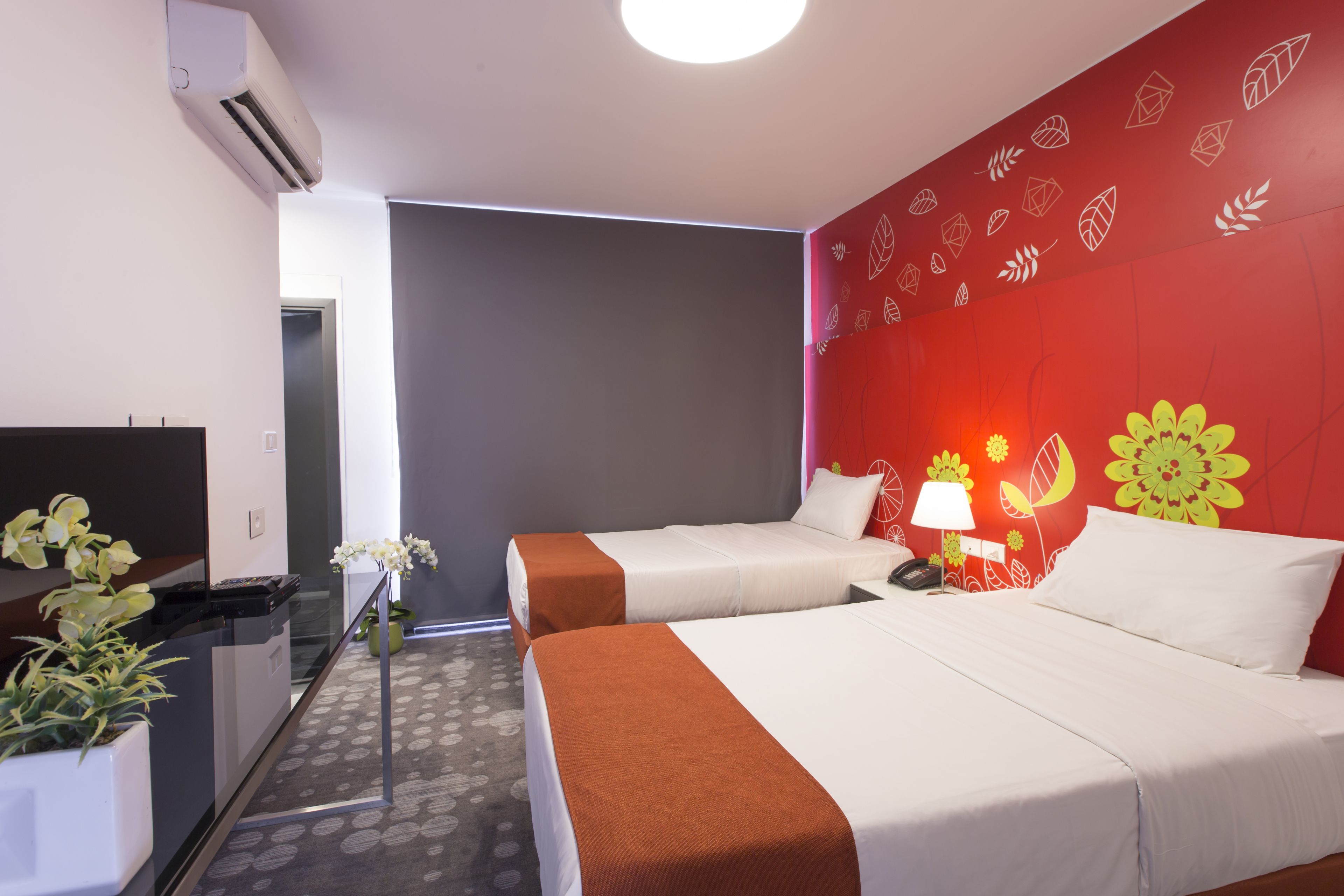 A hotel room with two beds, a desk, a TV, and a potted plant.
