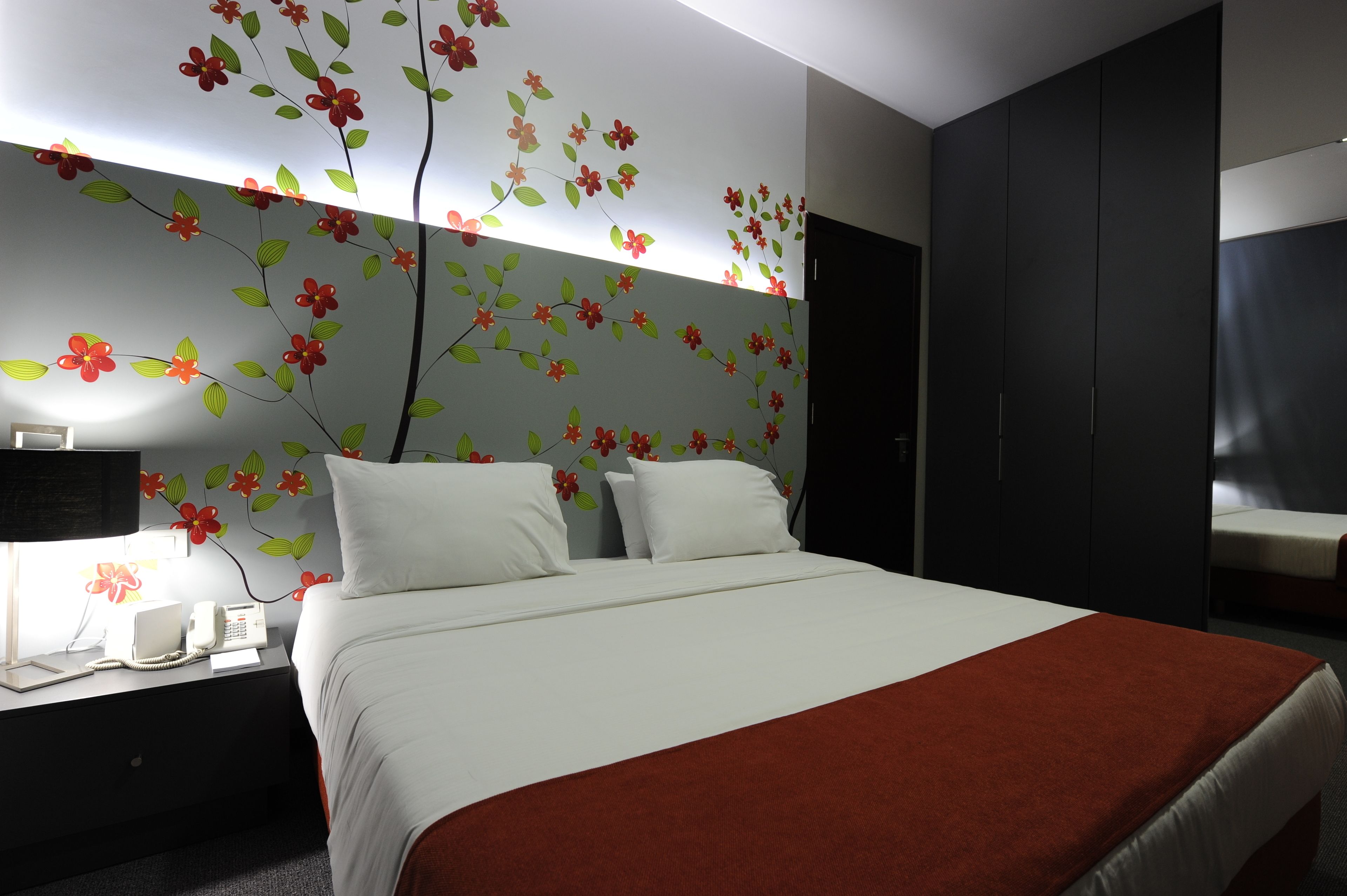 A modern hotel room with a large bed, a nightstand with a phone and lamp, and a wardrobe.