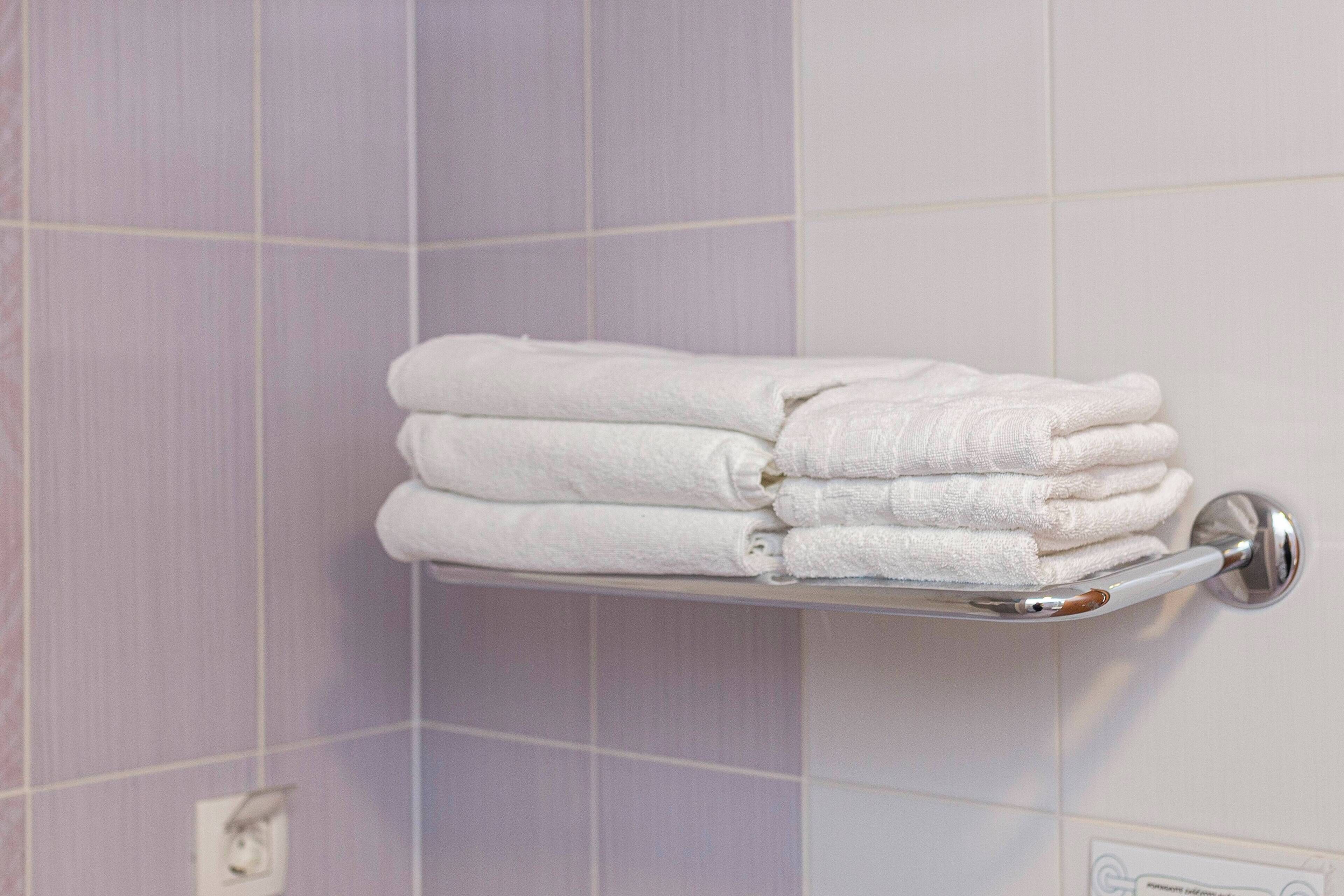 Een stapel witte handdoeken op een metalen handdoekhouder in een badkamer met paarse tegels.