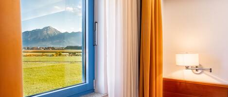 A hotel room with a large window offering a mountain view, a bedside lamp, and a wooden headboard.