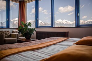 Habitació d'hotel amb un llit, una planta en test i una vista de muntanyes nevades a través de grans finestres.