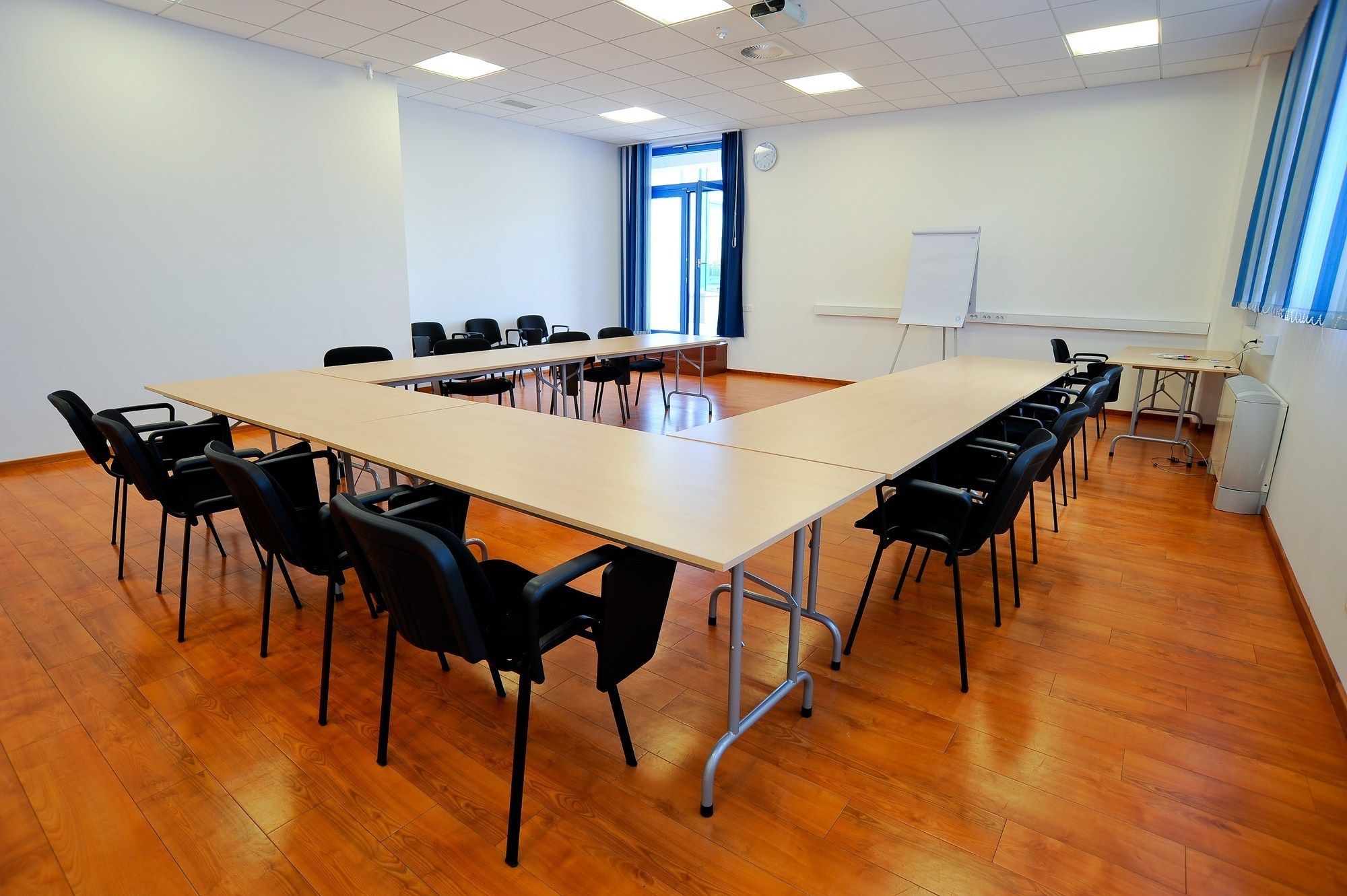 A conference room with a long table, black chairs, a whiteboard, and a clock on the wall.