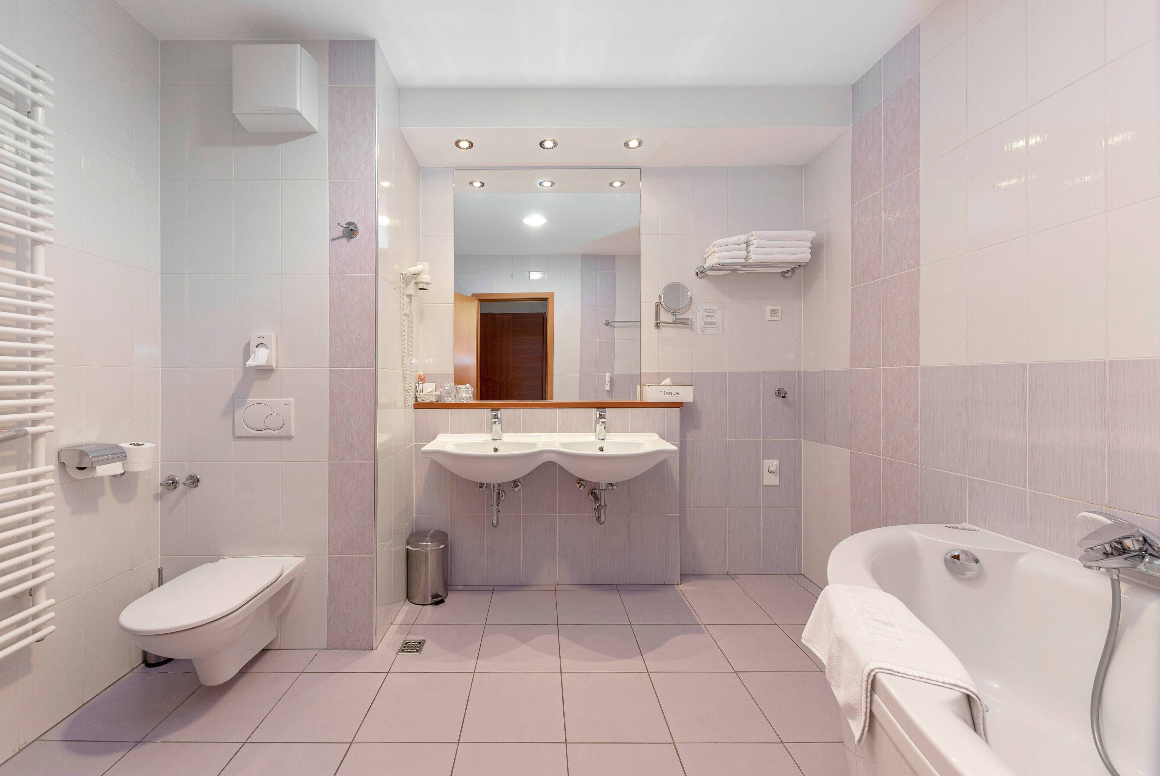 Un baño moderno con inodoro, dos lavamanos, un espejo y una bañera.