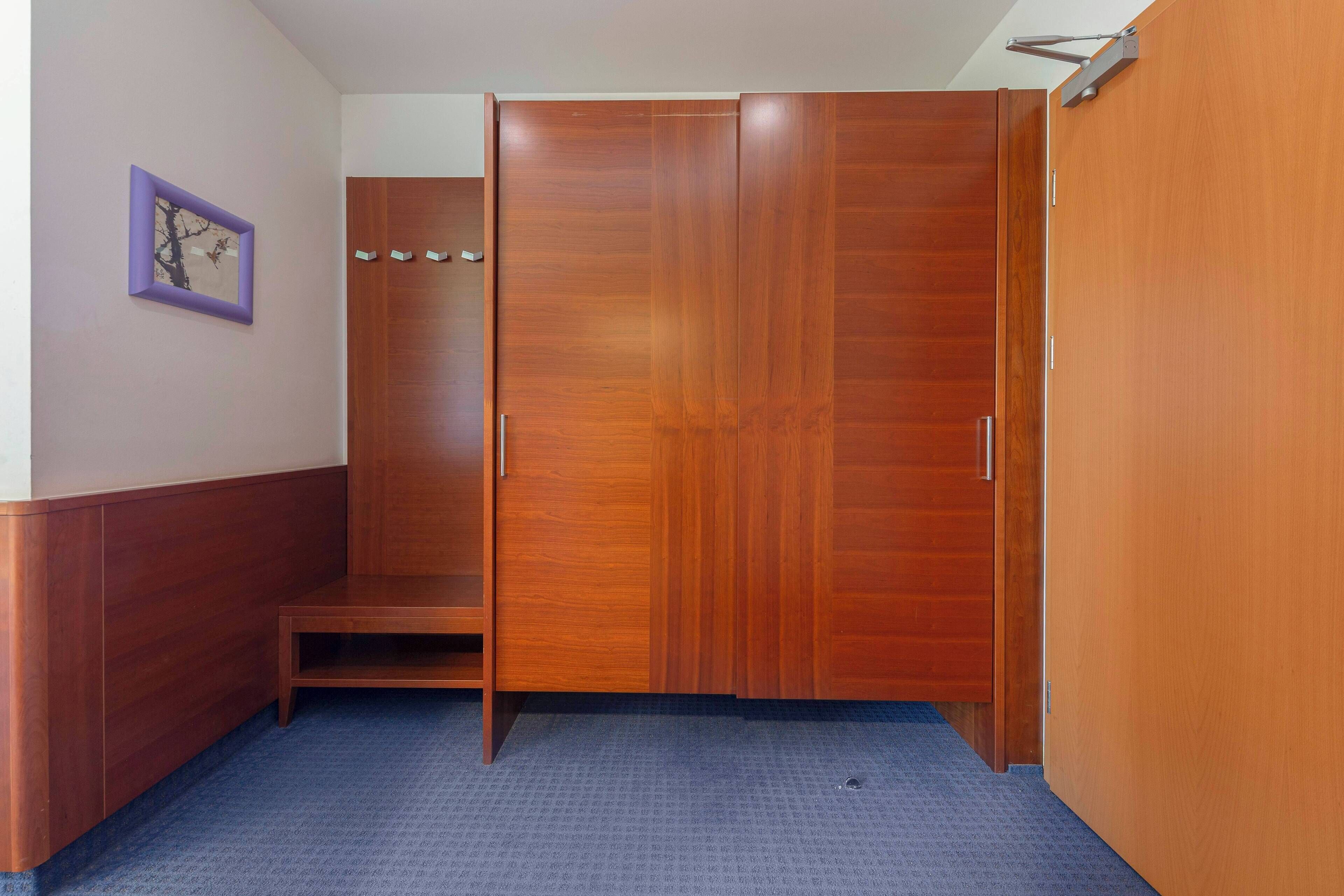 A room with a wooden wardrobe, a small bench, and a purple-framed picture on the wall.