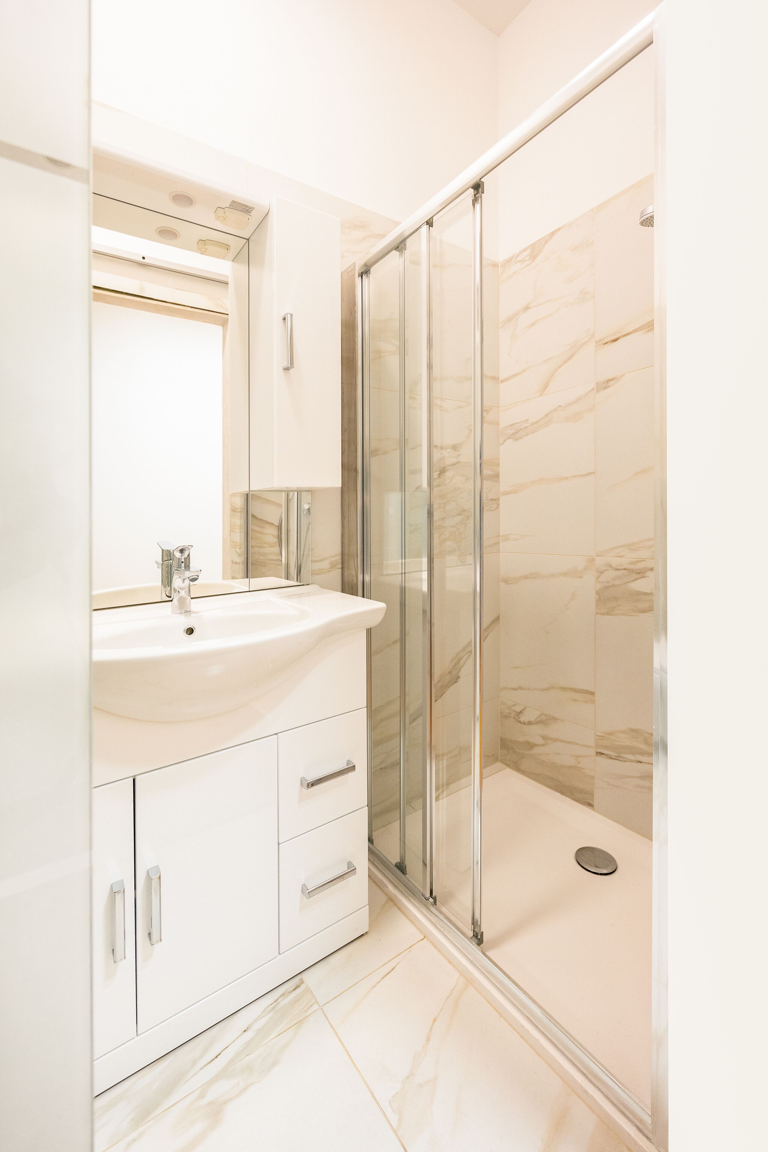 A modern bathroom with a white sink, mirror, and glass shower enclosure.