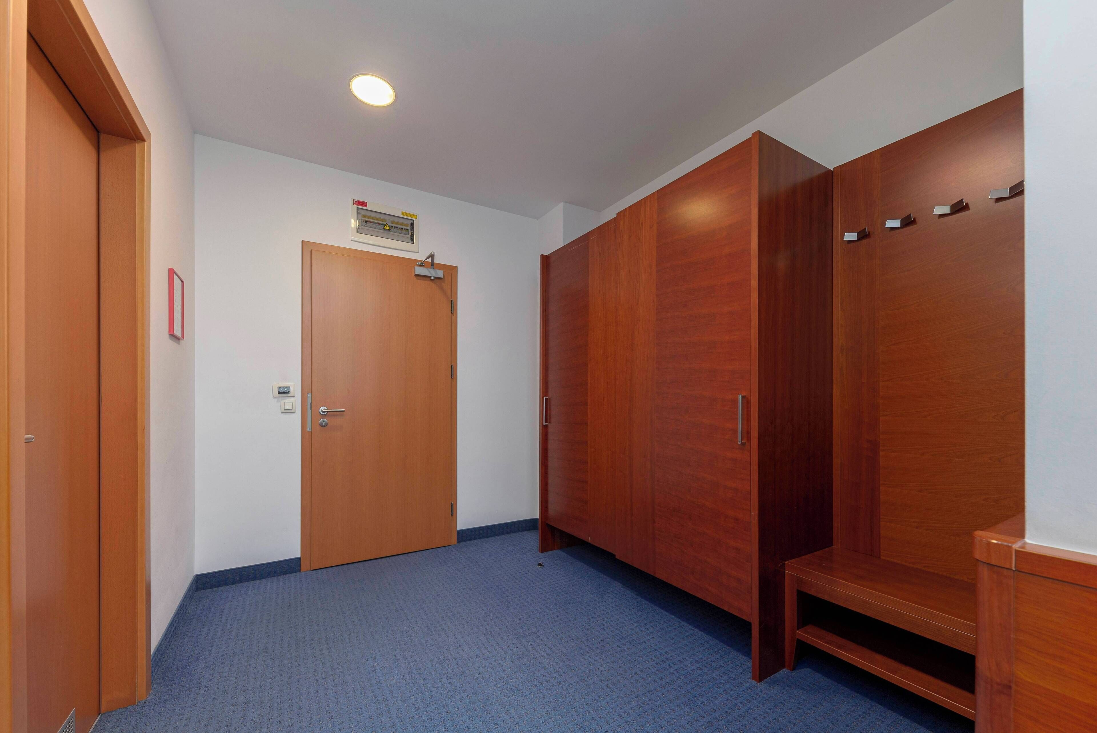 Een gang met een houten deur, een bank en een garderobe met haken.