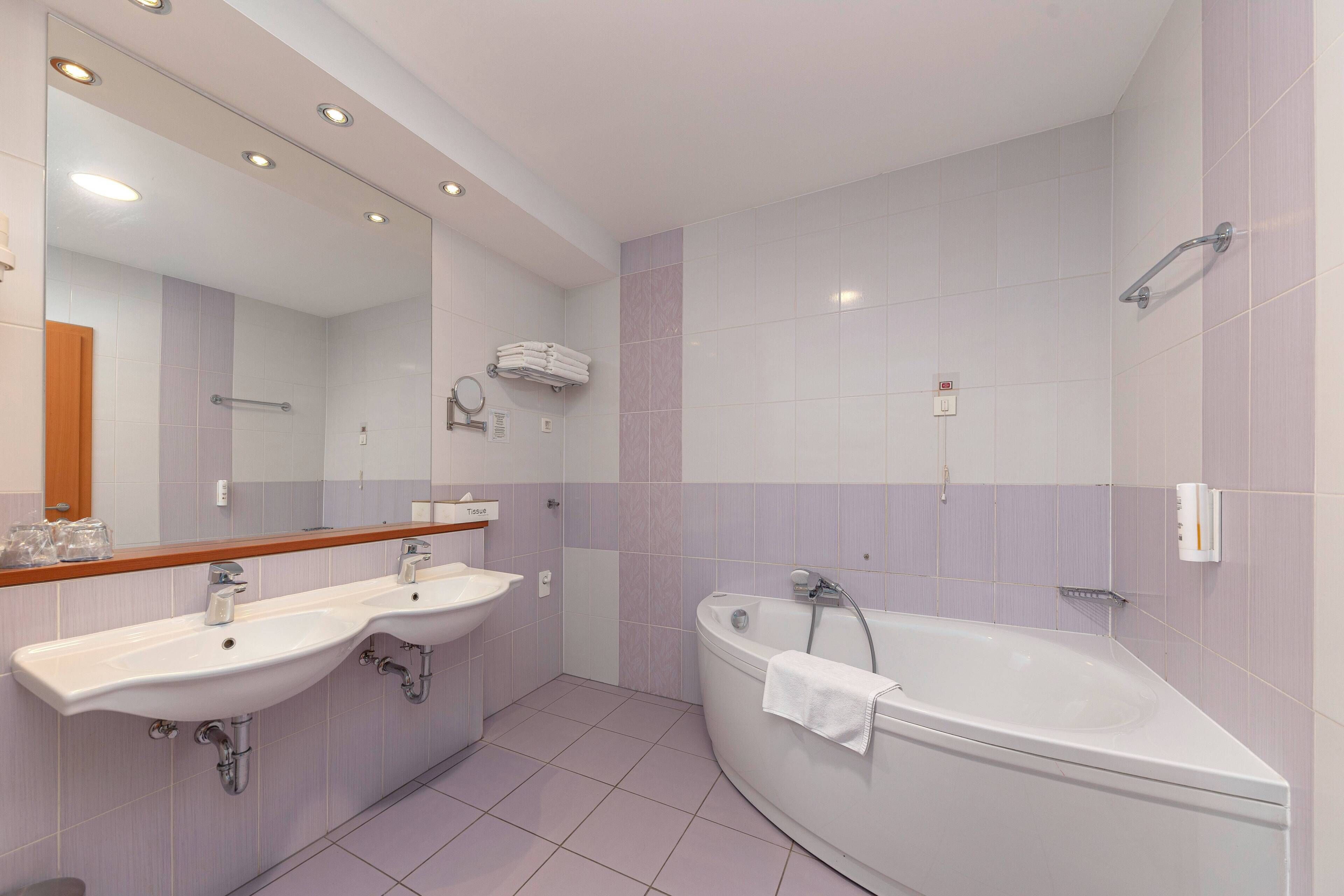 Une salle de bain moderne avec deux lavabos, une baignoire et un grand miroir.
