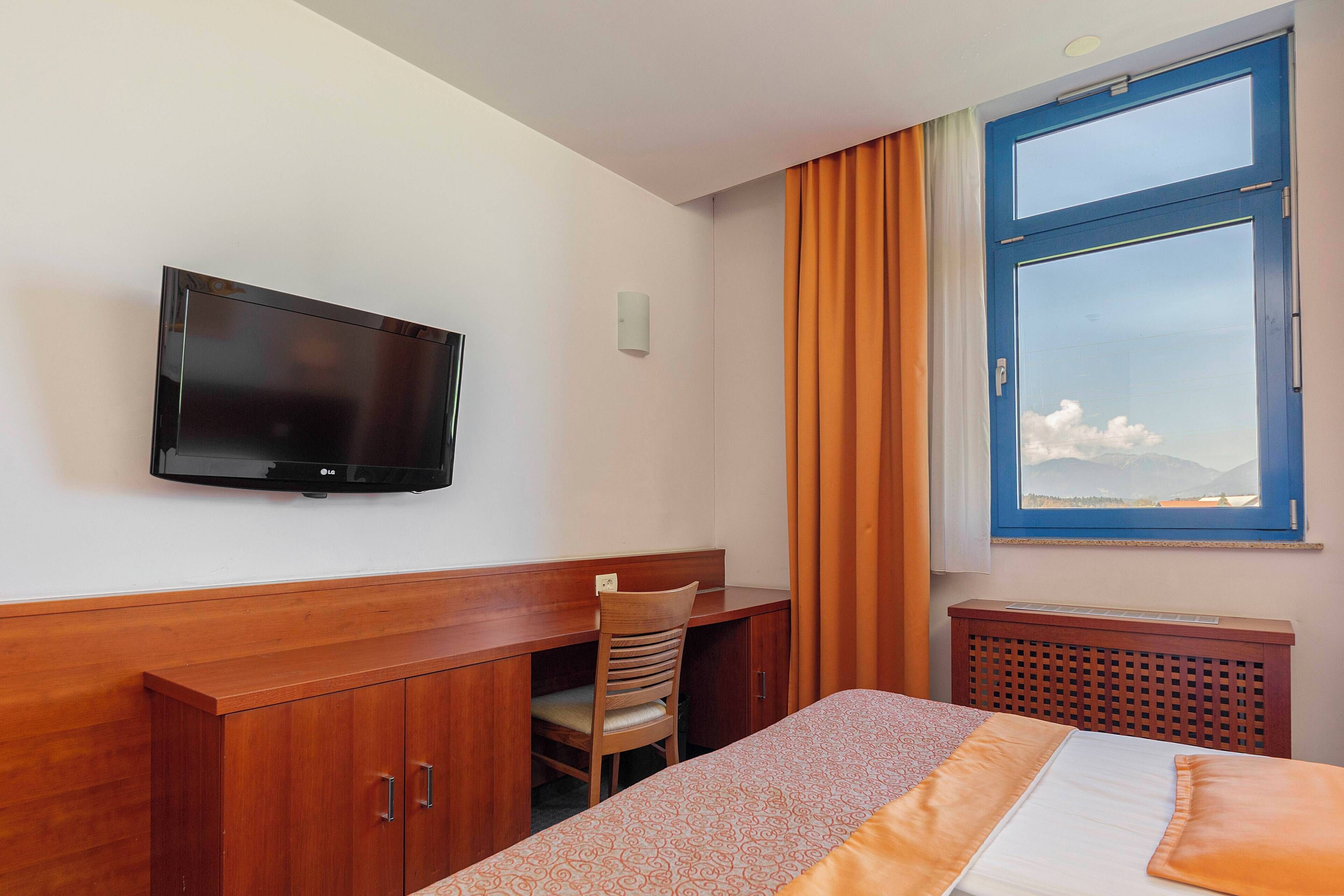 Une chambre d’hôtel équipée d’un lit, d’un bureau, d’une chaise, d’une télévision et d’une fenêtre donnant sur les montagnes.